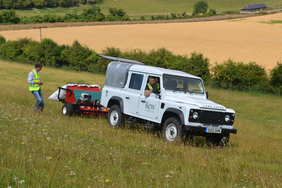 A brush-harvester being pulled behind a 4 wheel drive across a grassland slope