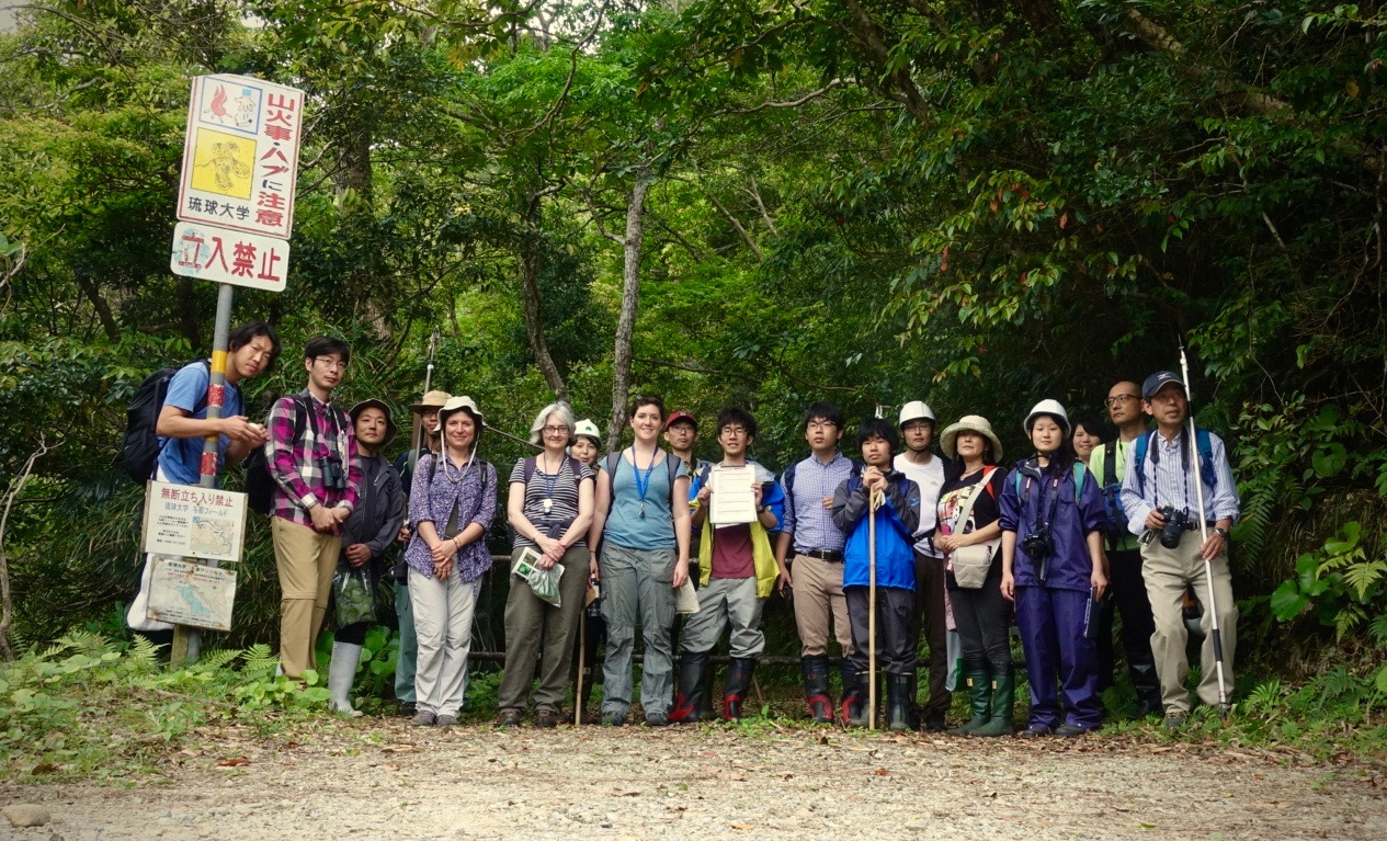 A group of people with seed collecting equipment standing in a row in front of a forest smiling