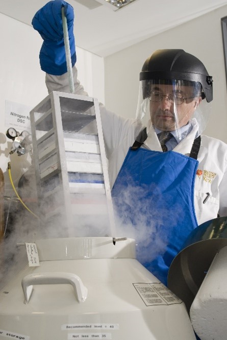 Keith in personal protective gear including face shield, gloves and an apron, removing a rack of samples from a cryo vessel